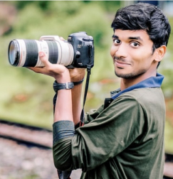 Sam, a young man holding a camera and grinning